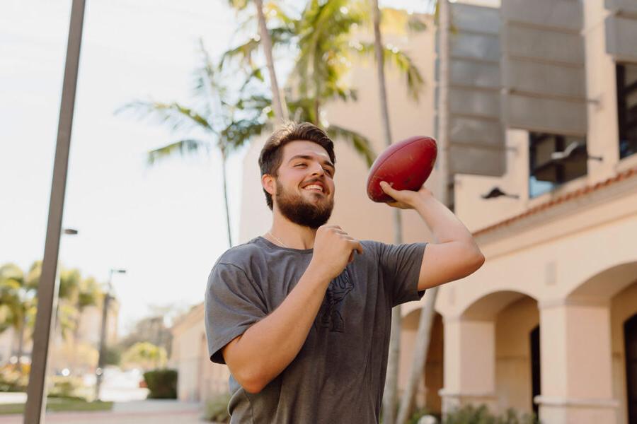 physical education student throws a football on campus.